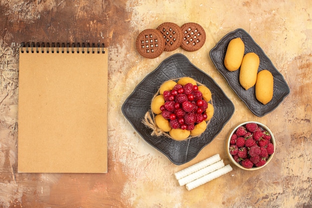 Una torta e biscotti del regalo sui frutti e sul taccuino marroni dei piatti sulla tavola di colore mista