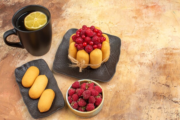 A gift cake and tea in a black cup with lemon and biscuits on mixed color table