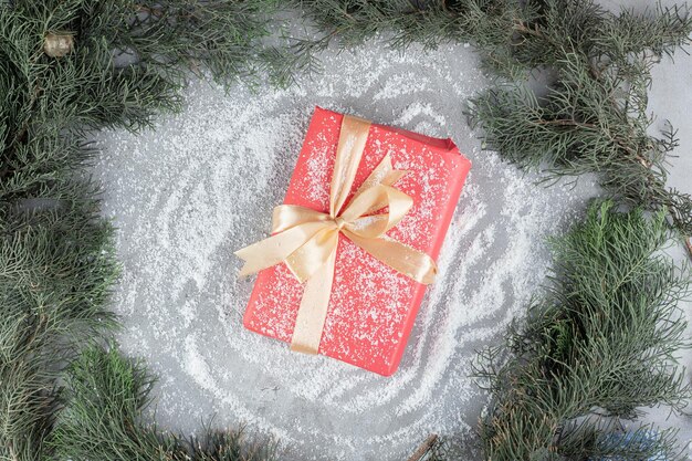 Gift package sitting on coconut powder amidst pine branches on marble table.