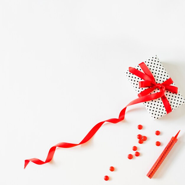 Gift tied with red ribbon near candies and sparkler candle on white background