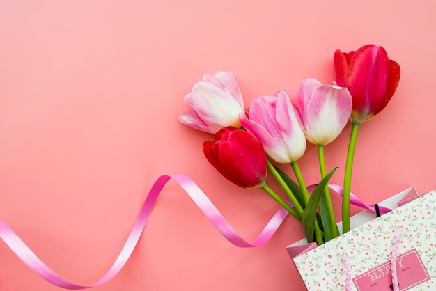 Gift with bouquet of flowers in bag on pink background