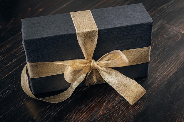 A gift wrapped in black paper and tied with a gold ribbon. expensive gift concept.