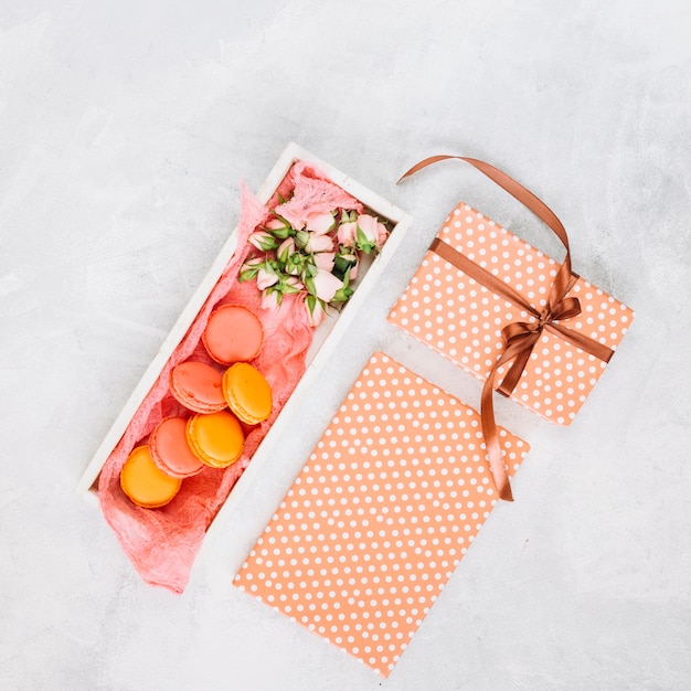 Gifts near box with macaroons and flowers