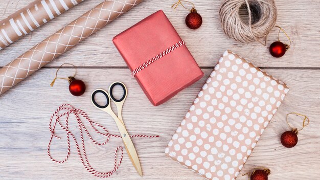Подарки в обертываниях вокруг рождественских шаров, ниток и ножниц