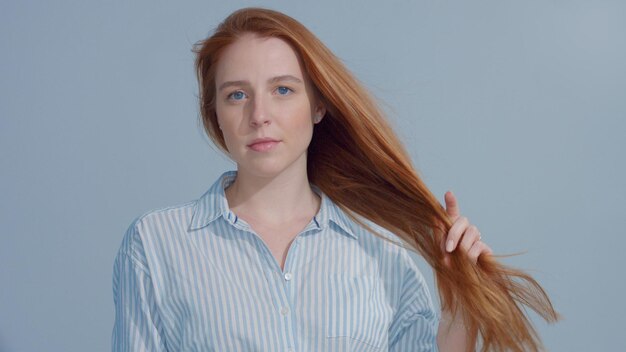 Ginger head red hair ginger hair model with blue big eyes in studio with blowing hair hold it in hand Beauty straight shiny hair blowing