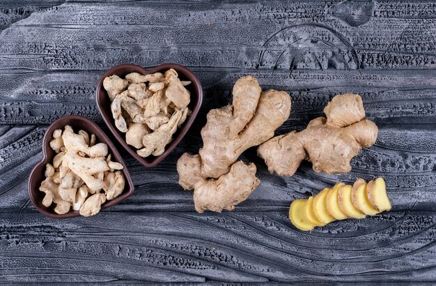 Ginger in heart shaped bowls with ginger slices top view on a dark wooden background