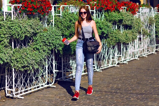 Рыжая хипстерская девушка проводит удивительный солнечный день на свежем воздухе, путешествует по Европе, повседневно выглядит хипстером, пьет вкусный кофе-латте на вынос, наслаждается отпуском и расслабляется.