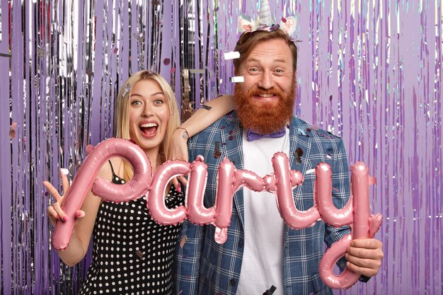 Ginger man and blonde woman at party holding balloons