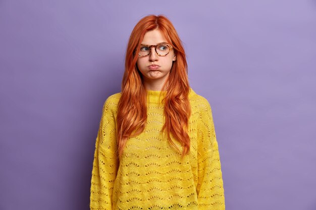 ginger offended young woman blows cheeks and makes unhappy grimace holds air has moody expression wears yellow sweater displeased with awful situation happened shows bad character