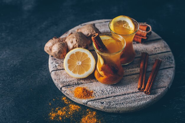 Ginger powder in tea cups with lemon, ginger and dry cinnamon high angle view on wood on a dark textured background