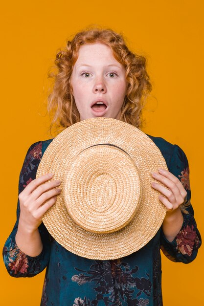 Ginger surprised young woman holding straw hat