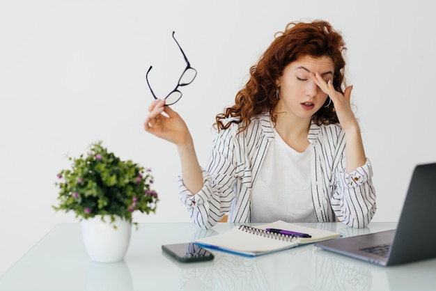 Ginger tired woman working on a laptop and drinking coffee Office archive accounting business