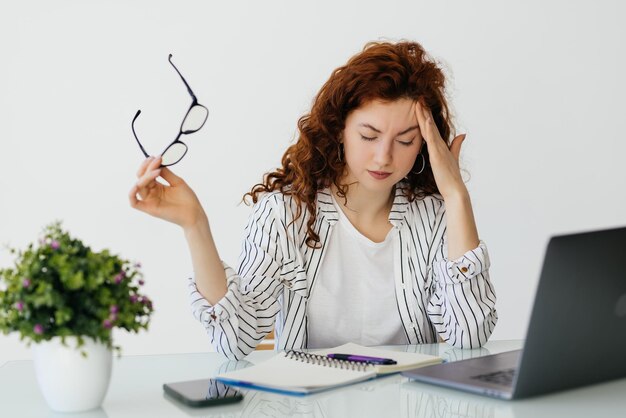 Ginger tired woman working on a laptop and drinking coffee Office archive accounting business