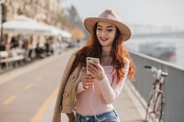 Donna bianca dello zenzero che sorride durante la lettura del messaggio mobile