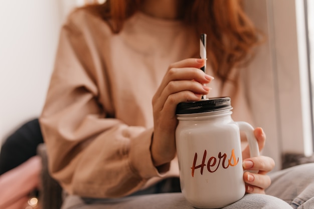 Ginger woman holding big cup of coffee. Stunning female model enjoying mulled wine at home.