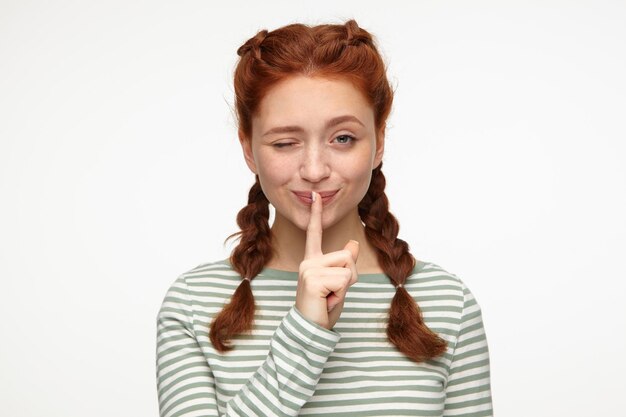Free photo ginger young female smiling wink and shows silence gesture