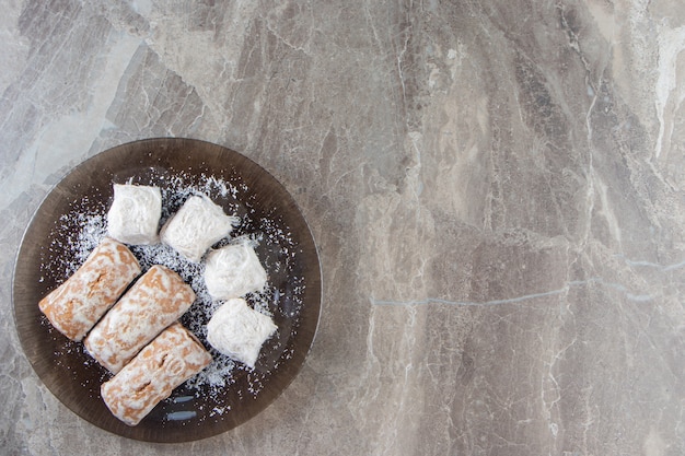 Free photo gingerbread with jam in sugar glaze and cotton candies on a plate on marble.