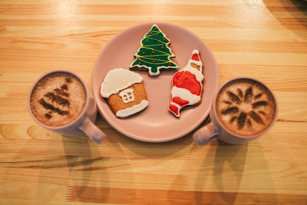 Gingerbreads with Christmas design lie on pink plate between cups with coffee