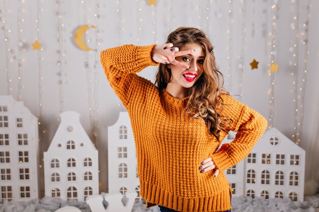 Girl of 25 years old with curly hair and blue eyes, posing showing peace sign. Portrait of attractive slavic model in magnificent interior