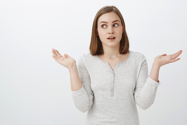 Girl acting clueless in front of parents. Portrait of cute emotive european female brunette shrugging with hands spread aside turning away while lying making unaware and uncertain expression