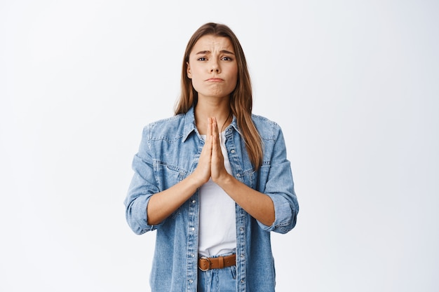 Girl apologizing, making clingy sad face and pleading you, standing against white wall