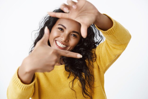 Girl artist searching inspiration in surroundings showing frames gesture and looking through make form shape of camera lens and smiling broadly standing white background enthusiastic