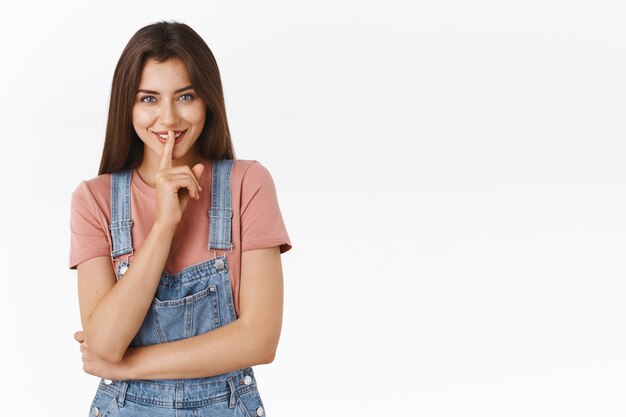 Girl asking not tell anyone her dirty little secret giggle mysteriously and smiling, press index finger to lips as have something to hide, standing white background prepare interesting surprise