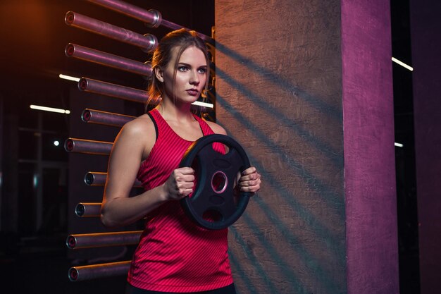 Girl athlete keeps the disc from the bar weighting agent for doing crossfit and fitness. Concept of sports equipment and weight loss.