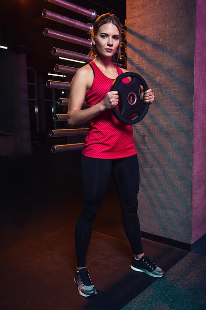 Девушка-спортсменка держит диск от утяжелителя штанги для занятий кроссфитом и фитнесом. Концепция спортивного инвентаря и потери веса.