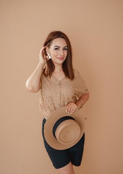 A girl in a beige shirt on a beige background holding a hat in her hands