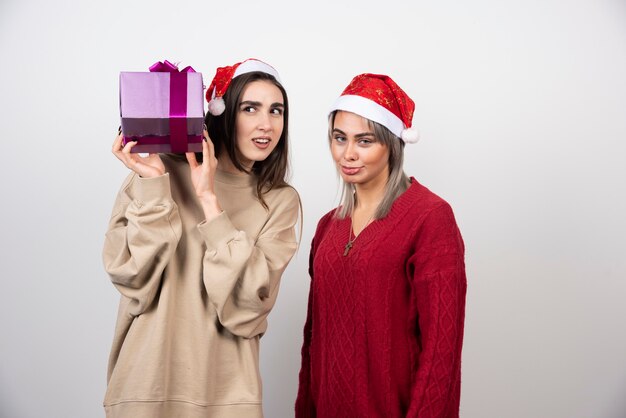Girl in beige sweater holding a present near a girl in red sweater .