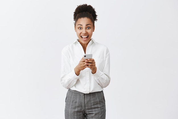 Girl being overwhelmed and excited reading incredible offer received via internet, checking mailbox in smartphone, staring amazed, standing over gray wall in suit