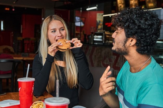 Девушка кусает бургер в кафе со своим парнем.