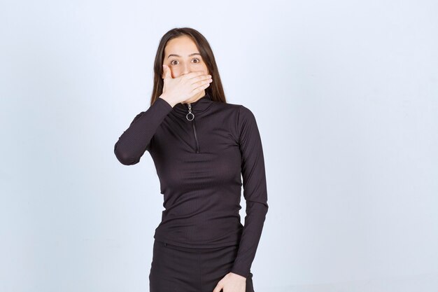 Girl in black clothes covering her mouth with hand. 