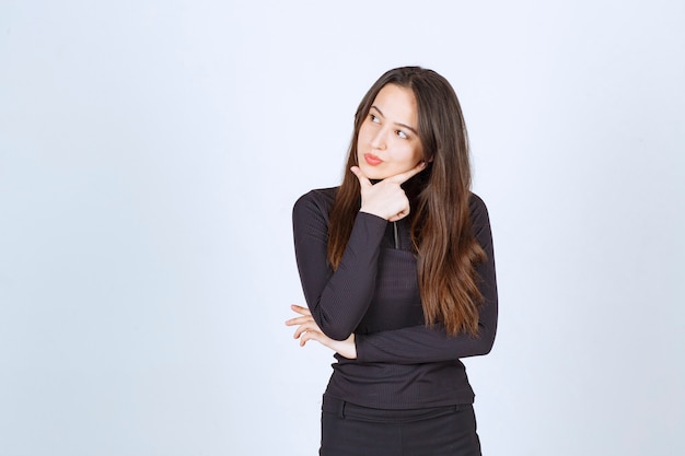 Girl in black clothes looks thoughtful and doubtful. 