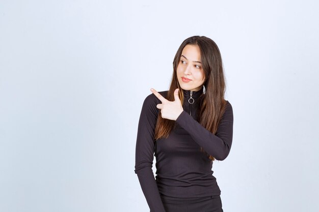 Girl in black clothes pointing at something on the left. 