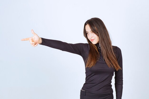 Girl in black clothes pointing at something on the left. 