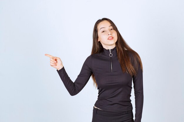 Girl in black clothes pointing at something on the left. 