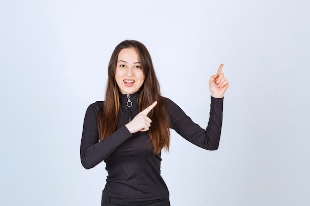 Girl in black clothes pointing at something on the right. 