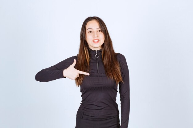 Girl in black clothes pointing at something on the right. 