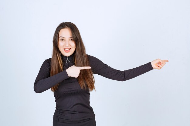 Girl in black clothes pointing at something on the right. 