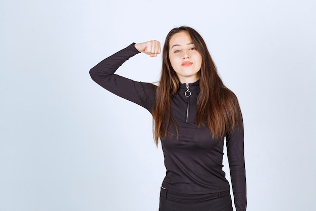 Girl in black clothes showing her fist and arm muscles. 