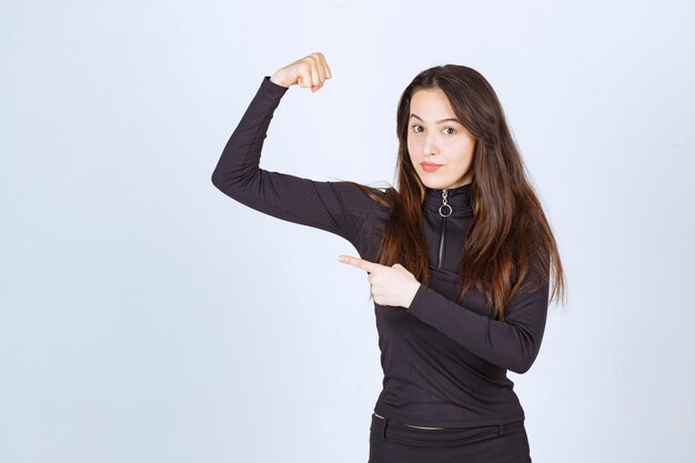 Girl in black clothes showing her fist and arm muscles. 