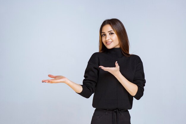 Ragazza in camicia nera che indica qualcosa a sinistra. foto di alta qualità