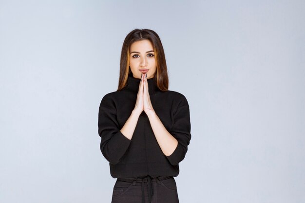 Девушка в черной рубашке, объединив руки и молясь. Фото высокого качества