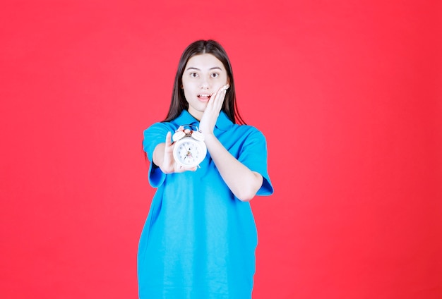 Girl in blue shirt holding an alarm clock and realizing she is late