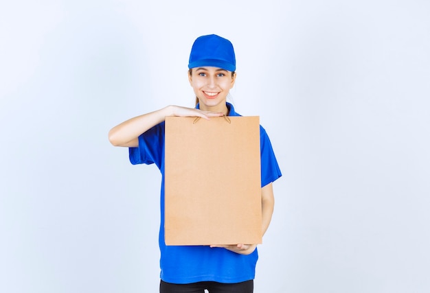 Девушка в синей форме держит картонную хозяйственную сумку.
