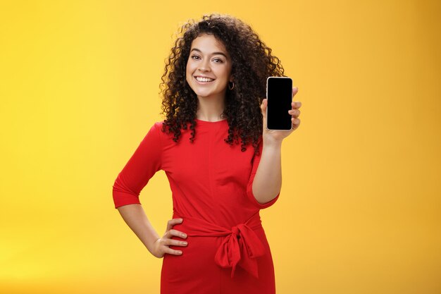 Девушка хвастается новым телефоном, купленным на Рождество, чувствуя себя счастливой, держа в руке мобильное устройство ...