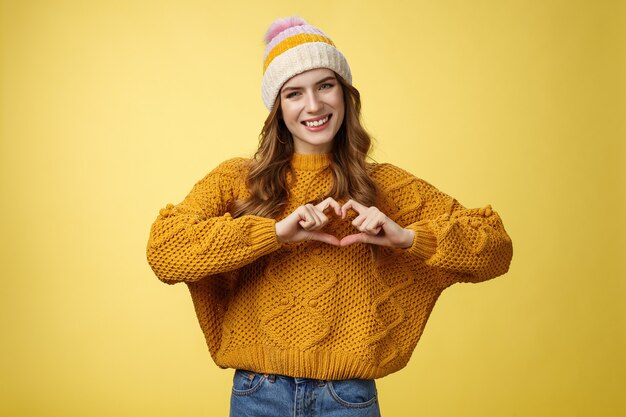 Girl brings peace love show heart gesture tilting head friendly smiling expressing sympathy passion confessing boyfriend warm feelings, heartbit sign, grinning flirty, standing yellow background