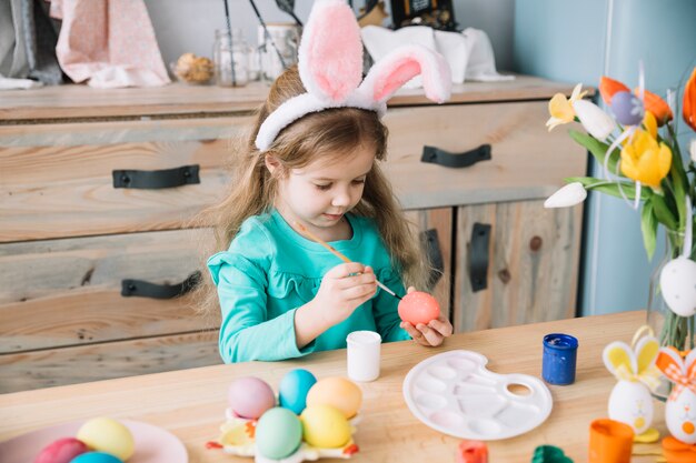 Girl in bunny ears painting eggs for Easter